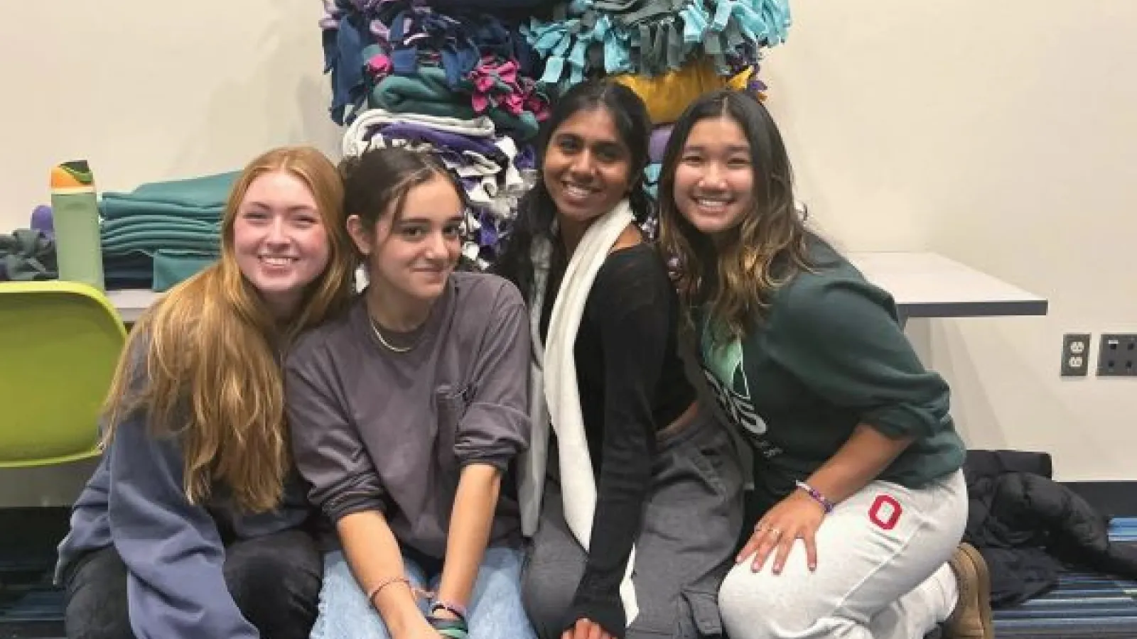 four students pose for the camera in front of a pile of fleece blankets
