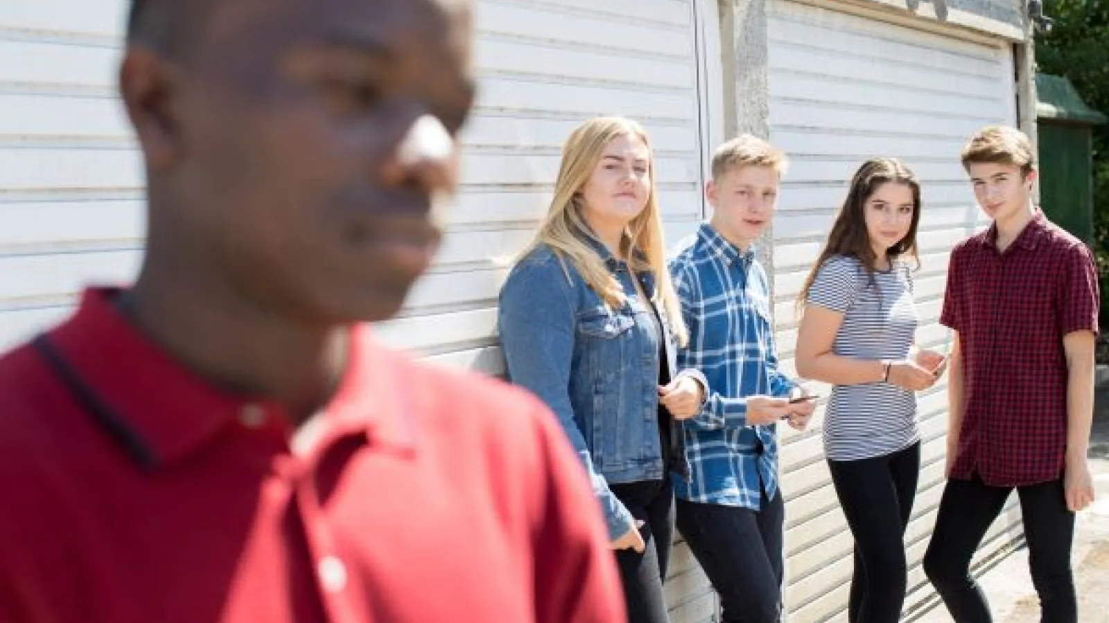 a group of white teens looks sideways at a black boy
