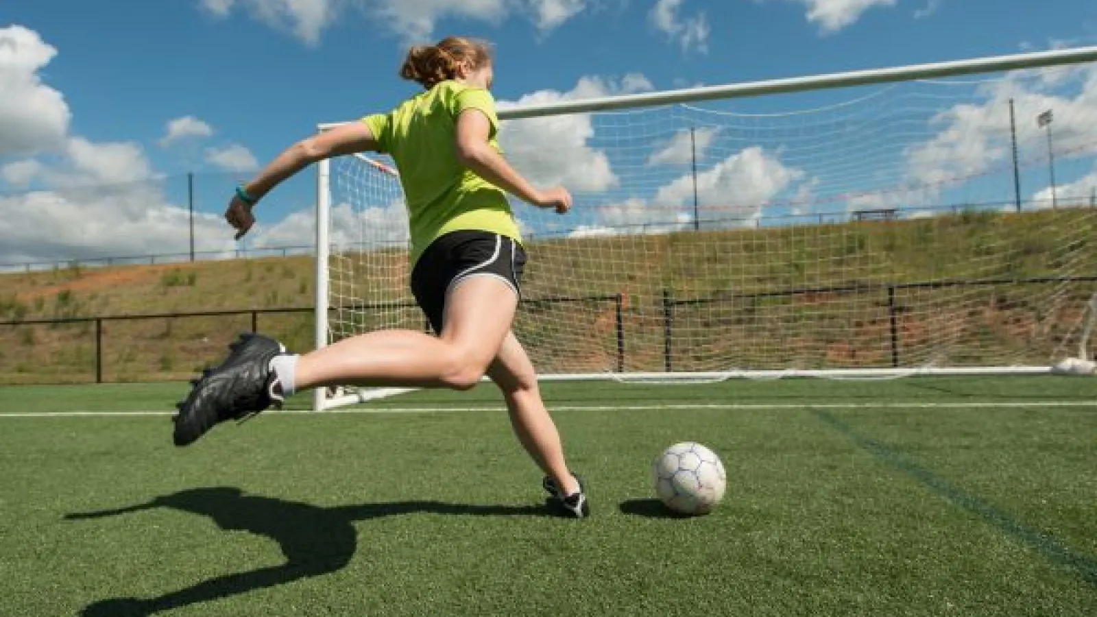 a young woman kicks a ball at a soccer goal