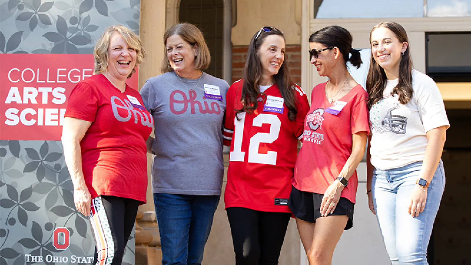 Five women wearing Buckeye shirts smiling on the steps of University Hall