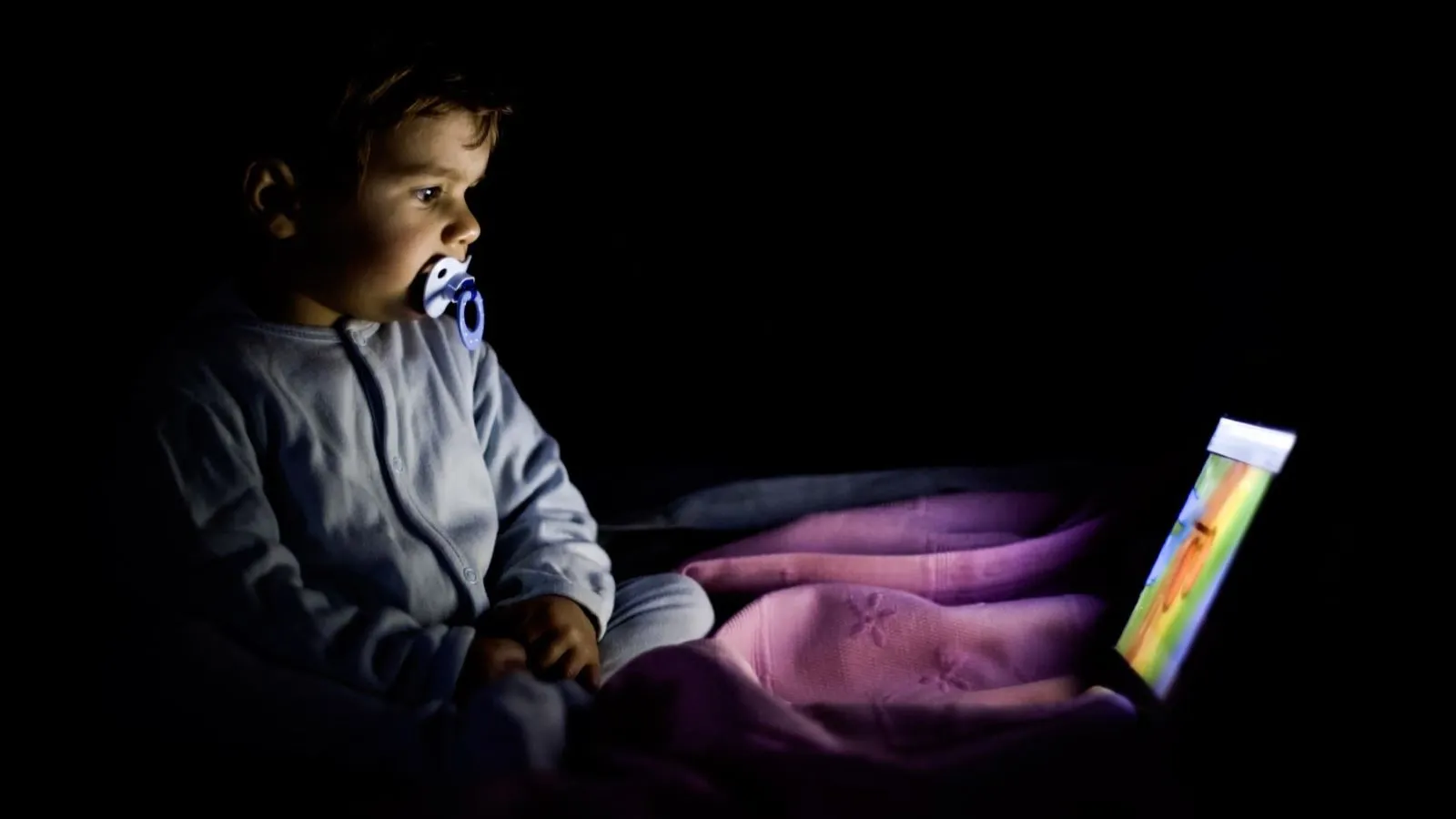a small toddler looking at an ipad in a dark room