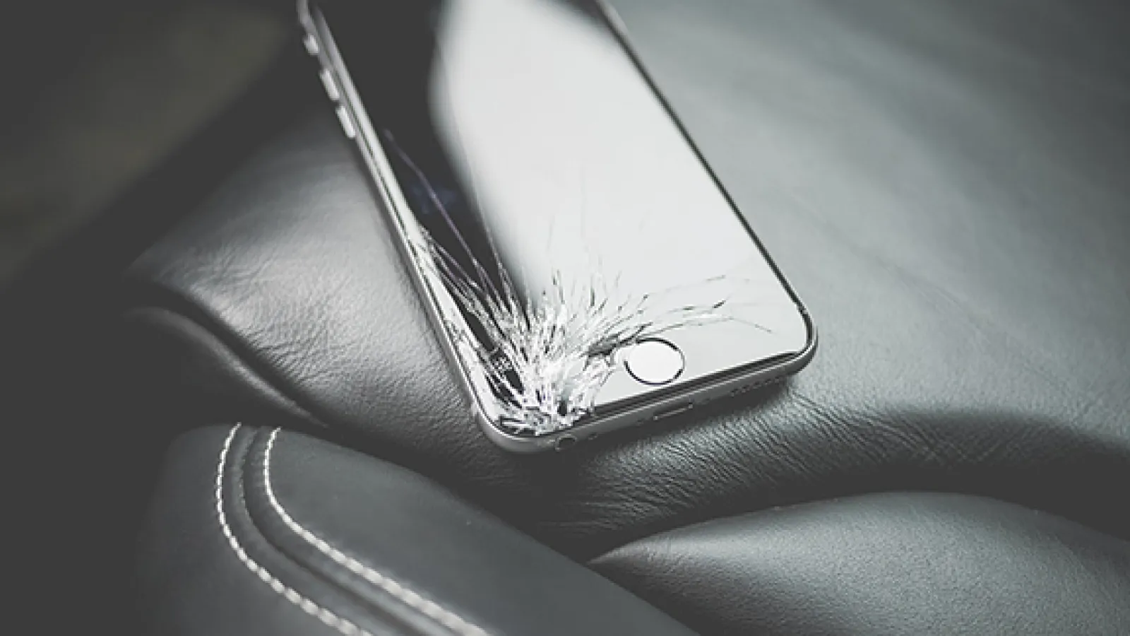 A cellphone with a cracked screen sits on a car seat
