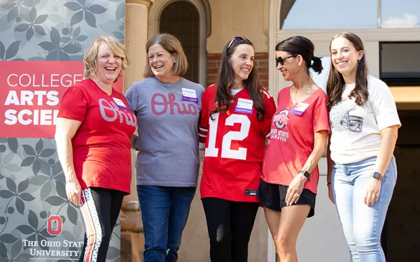 Five women wearing Buckeye shirts smiling on the steps of University Hall