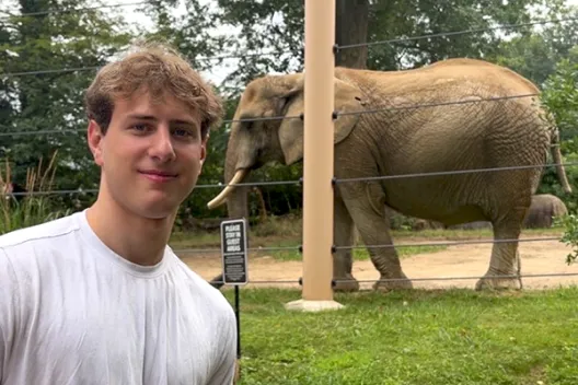 Connor stands next to an elephant in a wildlife reserve