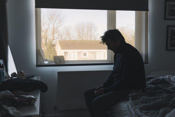 a man sits on a bed, head down and obviously sad