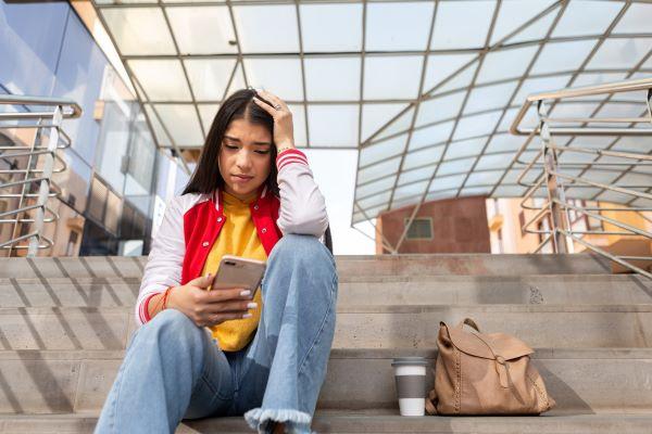 a young woman with dark hair looks sadly at her phone