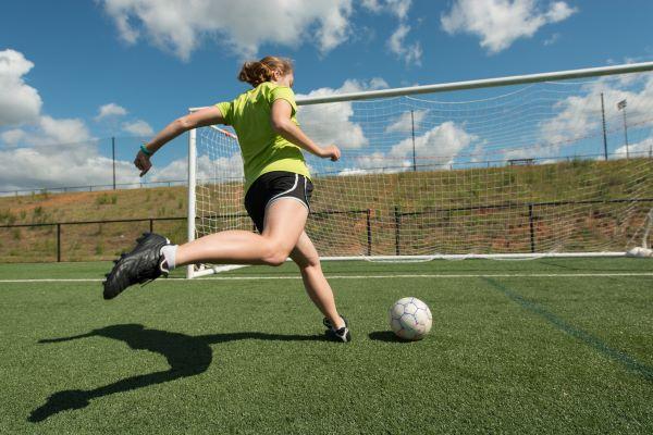 a young woman kicks a ball at a soccer goal