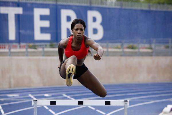 a young black woman running hurdles on a college track