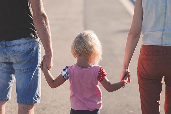 Parents hold hands with their young child on a beach