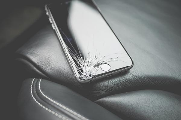 A cellphone with a cracked screen sits on a car seat A cellphone with a cracked screen sits on a car seat